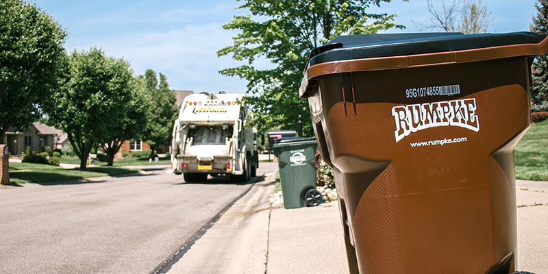 Rumpke Waste pickup truck and trash cart on a residential street